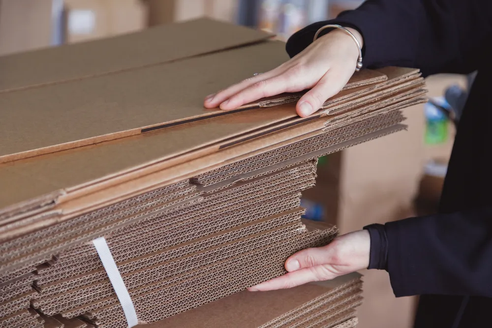 Vista superior de varias cajas de cartón Querétaro de distintos tamaños, apiladas sobre un piso de madera con tonos grises. 